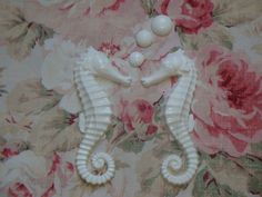 two white seahorses sitting on top of a flowered wallpaper covered ground