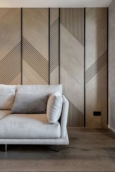 a white couch sitting in front of a wooden wall with geometric designs on it's walls