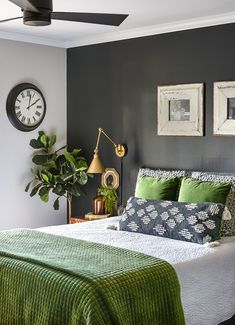 a bedroom with green and white bedding, pictures on the wall and a clock above it