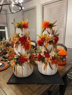 two white pumpkins decorated with orange and red flowers on top of a wooden table