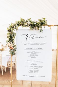 an elegant welcome sign with greenery and flowers on it is displayed in front of a white tent