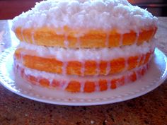 a three layer cake sitting on top of a white plate covered in icing and coconut