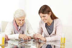 an elderly woman playing board games with her companion at the glass table in front of them