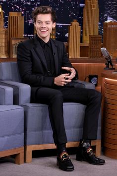 a man sitting on top of a blue couch in front of a tv screen wearing black shoes