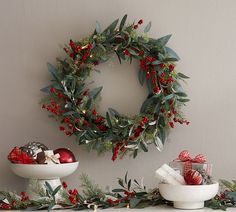 a wreath on the wall above two white bowls filled with christmas decorations