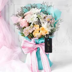 a bouquet of flowers is wrapped in blue paper and tied with a pink ribbon, sitting on a white surface