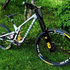 a mountain bike parked in the grass next to some bushes and trees with yellow letters on it