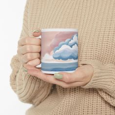 a woman holding a coffee mug with clouds painted on the front and sides in her hands