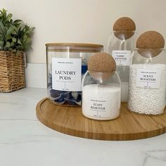 three jars filled with different types of bath salts on top of a wooden tray next to a potted plant