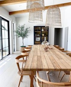 a dining room table with chairs and lights hanging from it's ceiling in front of large windows