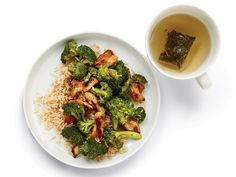 a white plate topped with chicken and broccoli next to a cup of tea