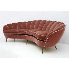 a curved couch with wooden legs and a pink velvet upholstered back, sitting on a white floor