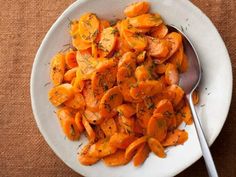 a white plate topped with sliced carrots on top of a wooden table next to a fork