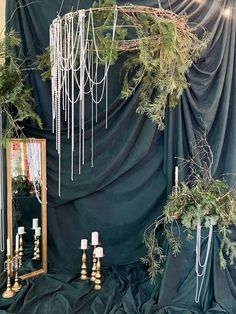 an arrangement of greenery and candles are on display in front of a curtained backdrop