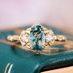 an oval shaped blue and white diamond ring on top of a green leather book with gold trim