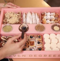 a pink box filled with lots of different types of pastries and desserts on top of a table