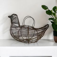 a wire chicken sitting on top of a white shelf next to a potted plant