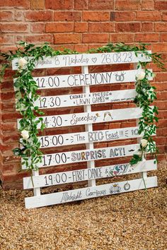 a wooden sign is decorated with flowers and greenery for an outdoor wedding ceremony in front of a brick wall