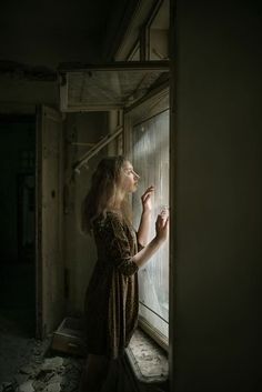 a woman standing in front of a window with her hand on the window sill