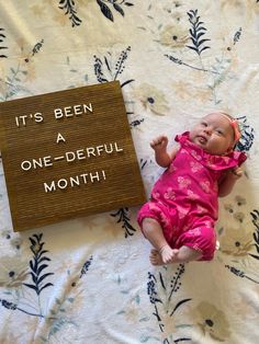 a baby doll laying on top of a bed next to a sign that says it's been a one - derful month