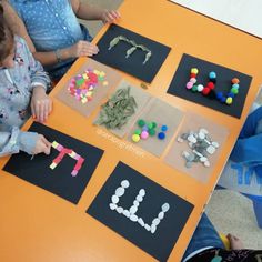 two children sitting at a table making letters out of construction paper and colored beads on them