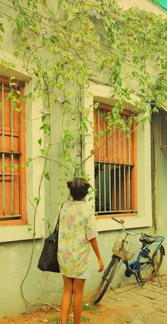 a woman standing in front of a building with a bike parked next to the window