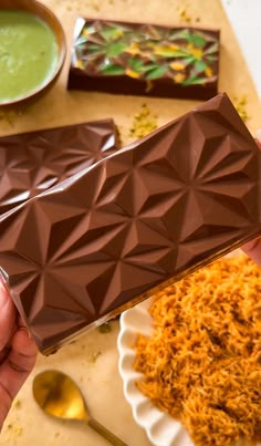 a person holding a chocolate bar in front of some bowls and spoons on a table