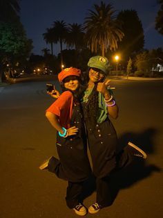 two people standing in the middle of a street at night with palm trees behind them