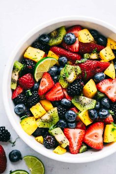 a white bowl filled with fruit and topped with kiwi, strawberries, lemons, blueberries, raspberries