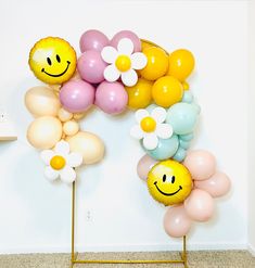 balloons are arranged in the shape of flowers and smiley faces on stands against a white wall