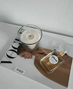 a magazine with a candle on top of it next to a glass vase and perfume bottle