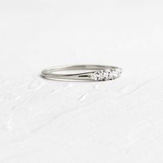 a three stone diamond ring sitting on top of a white surface with no one around it