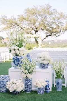 an outdoor ceremony setup with blue and white vases, flowers, and greenery