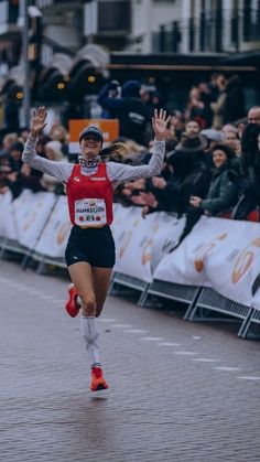 a woman running down a street with her arms in the air as she crosses the finish line