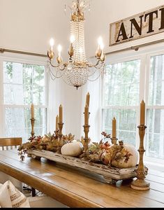 a dining room table with candles and pumpkins on it in front of two windows