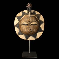 a wooden sculpture with a sun face on it's head and a black background