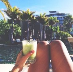 a person sitting on the beach with a drink in their hand and palm trees behind them