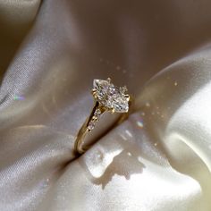 a diamond ring sitting on top of a white satin material with the light shining through it