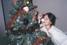 a woman sitting next to a christmas tree with ornaments on it and blowing bubbles in front of her face