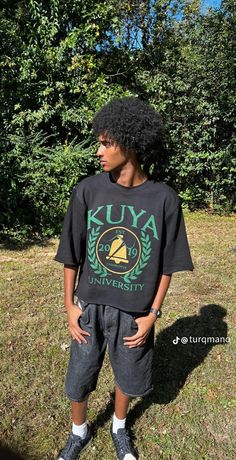 a young man standing in the grass wearing a black shirt with kuya university on it