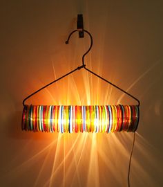 a multicolored light hanging from a metal hook on a wall with the sun shining through it