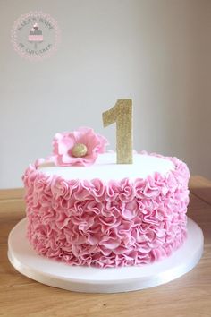 a cake with pink ruffles and a gold number one on top is sitting on a table