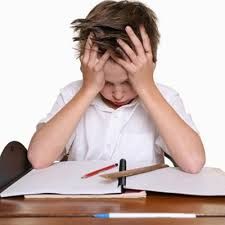 a young boy sitting at a desk with his head in his hands and writing on paper