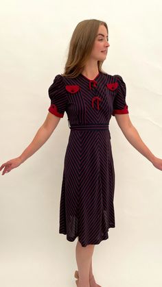 "This is a very special dress, it is so stylish! It is one of my favourite ever 1930s dresses that I have ever had in my collection. It dates from the late 1930s and is made from a navy blue coloured silk crepe with red chevron patterned striped highlights. The design features two faux pockets to the front bodice which are complemented by the red sleeve embellishments and piping to the neckline and pretty puffed sleeves. There are two ties to the front and it retains its original navy and red chevron striped belt at the waist. The dress opens and closes with press studs on one side at the waist and there are three press studs to the bodice so that you can wear the neckline open or closed. This is one of several dresses in my collection that came from a private family collection of antique Navy Fitted Vintage Dress, Navy Vintage Short Sleeve Dress, Vintage Navy Dress For Formal Occasions, Retro Navy Dress For Formal Occasions, Vintage Red Midi Dress For Evening, Navy Retro Dress For Formal Occasions, Navy Vintage Style Formal Dress, Navy Retro Formal Dress, Striped Highlights