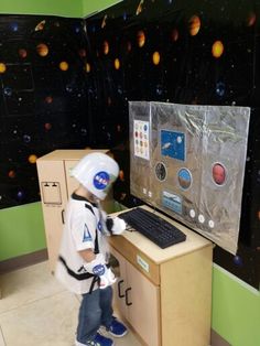 a young boy standing in front of a computer with planets on the wall behind him