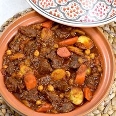 a bowl filled with stew and carrots on top of a woven place mat next to a plate