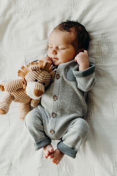 a baby laying on top of a bed next to a stuffed animal toy and wearing a sweater