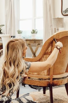 a woman sitting on the floor next to a wooden chair with her hand on it