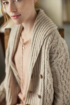 a woman sitting in a chair wearing a cardigan and looking off to the side