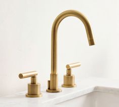 two brass faucets on a white counter top